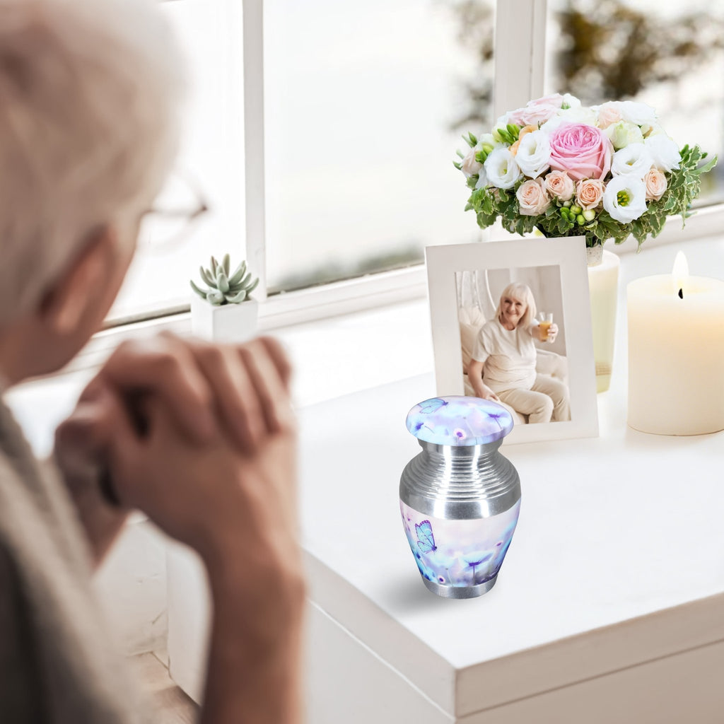 Small urns for human ashes with blue butterflies, tiny keepsake urn on windowsill, elderly lady in peaceful memorial moment