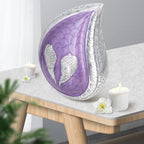 Purple engraved angel wings teardrop metal funeral urn placed on wooden side table with candles for home mantel decor