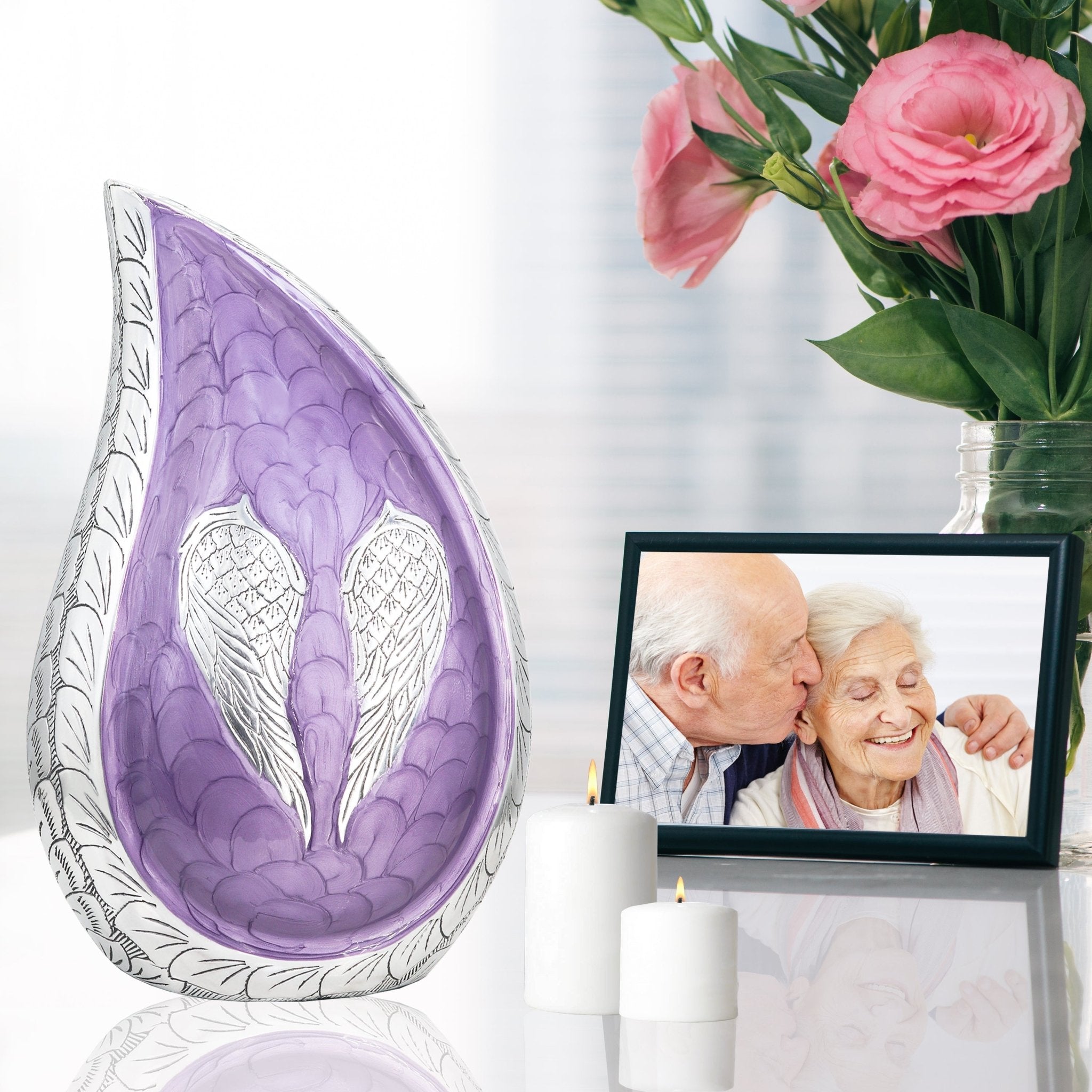 Purple angel wing teardrop cremation urns for adults set on reflective table with family photo and pink blooms
