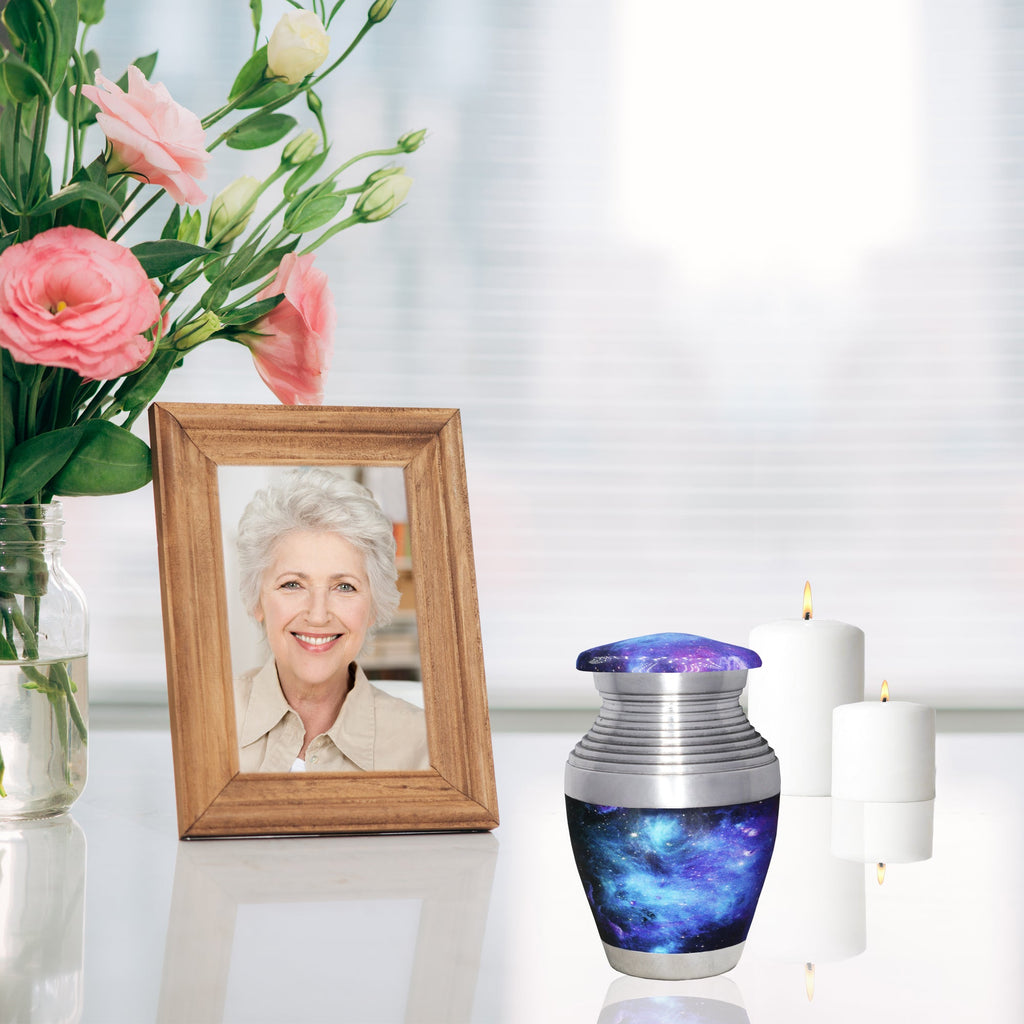 Ashes keepsake urn with blue cosmic galaxy design displayed beside a framed memorial photo and remembrance candles