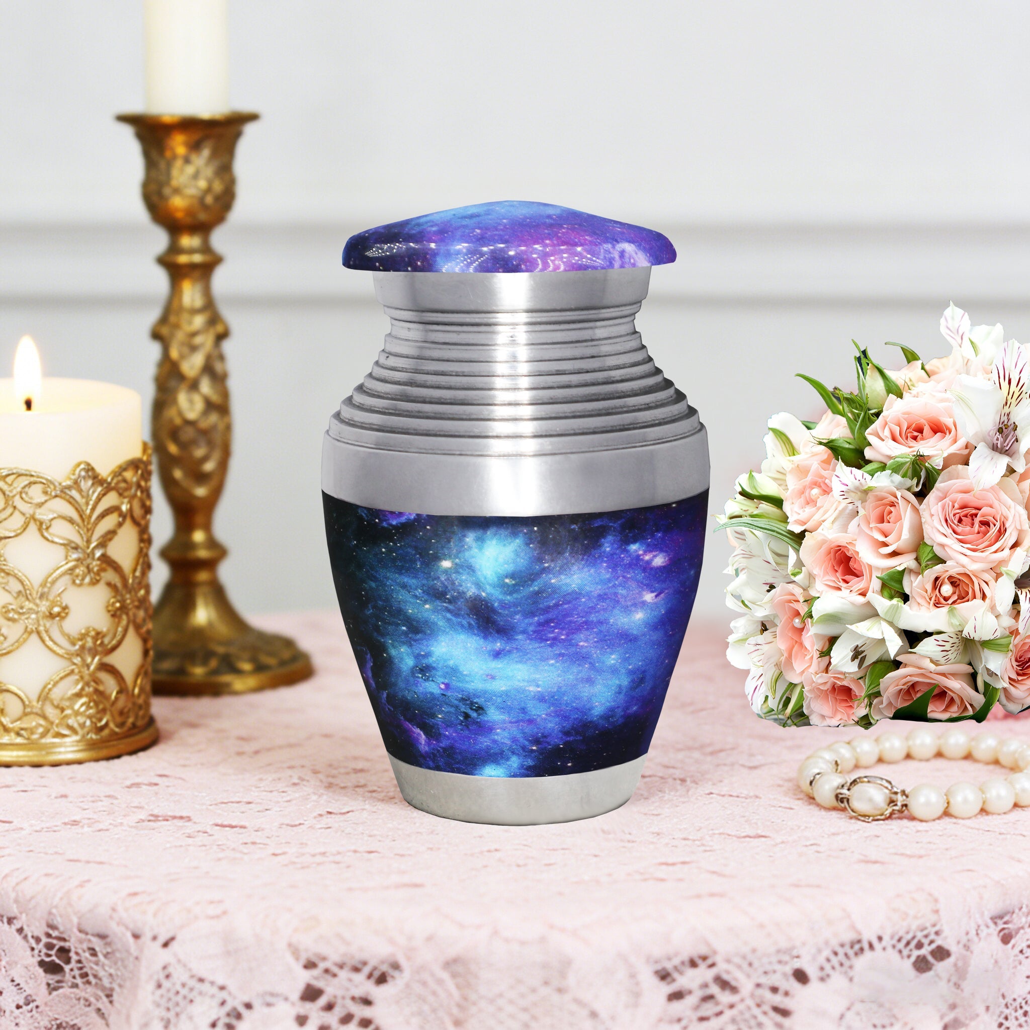 Miniature urn for ashes with blue cosmic galaxy artwork displayed with memorial flowers and an elegant gold candlestick