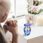 Small memorial urn for cremated remains with deep blue cosmic artwork displayed near an elderly woman at home