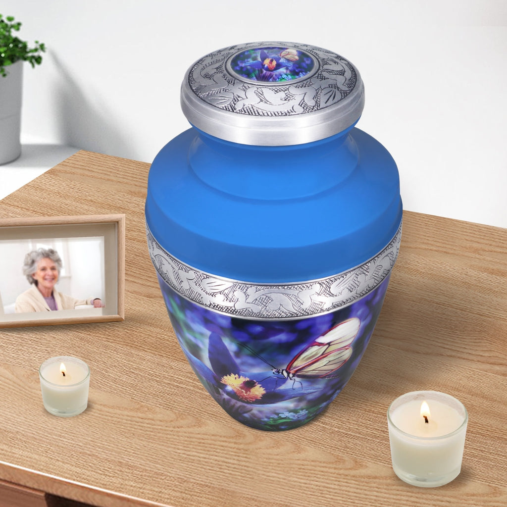 Urns for cremated remains beside candles, blue floral memorial for mother with engraved aluminum craftsmanship