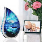 Aurora teardrop ash urn with turquoise finish on shiny table with couple photo, pink roses & memorial candles