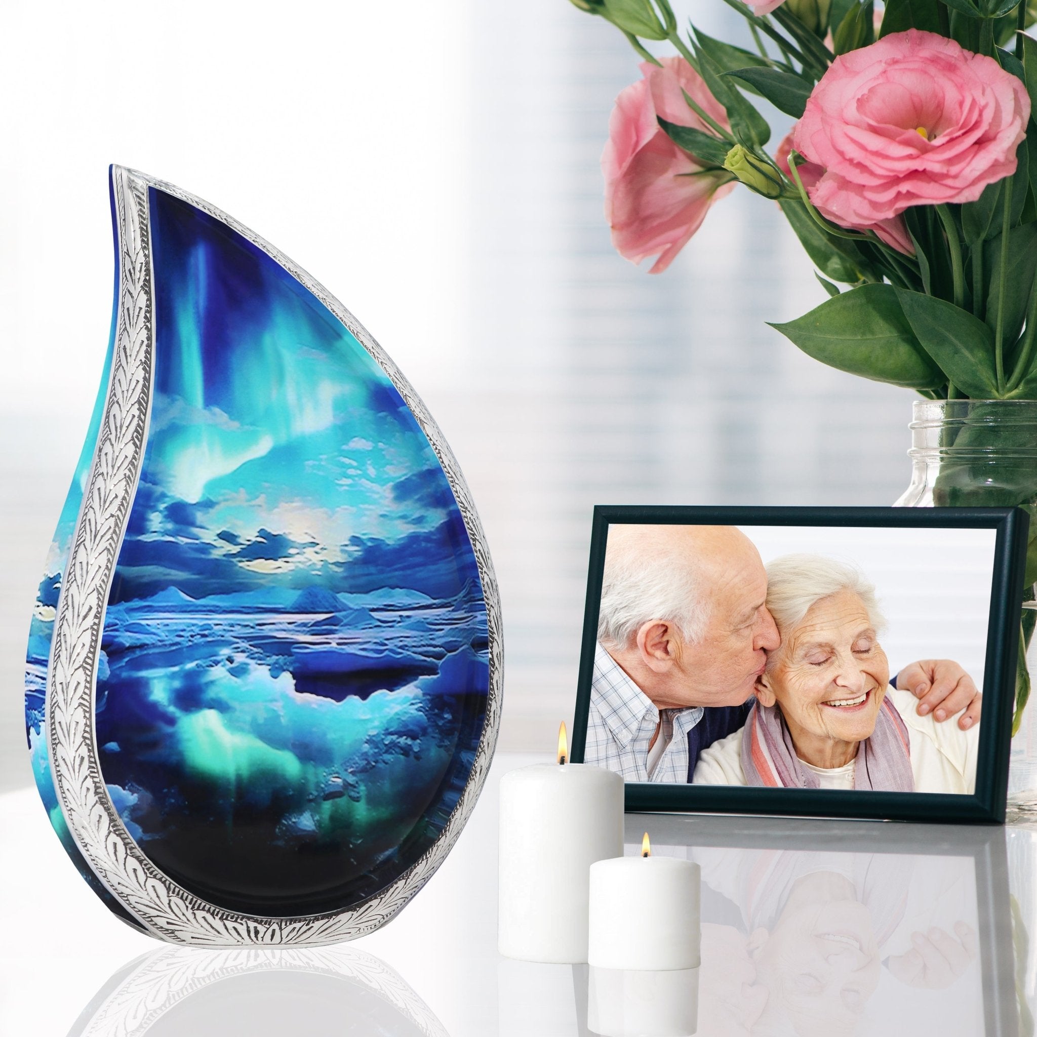 Aurora teardrop ash urn with turquoise finish on shiny table with couple photo, pink roses & memorial candles