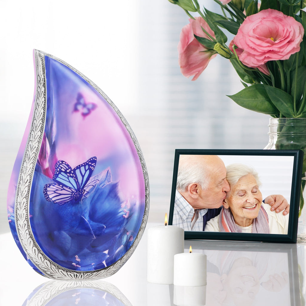 Pink blue butterfly aluminum adult urn set on reflective table beside family photo frame and soft memorial roses