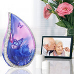 Pink blue butterfly aluminum adult urn set on reflective table beside family photo frame and soft memorial roses