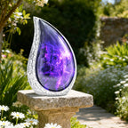 Purple cosmic galaxy burial urn displayed outdoors on a garden stone among green foliage