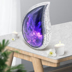 Modern amethyst-inspired urn with cosmic galaxy artwork displayed on a home memorial shelf with greenery