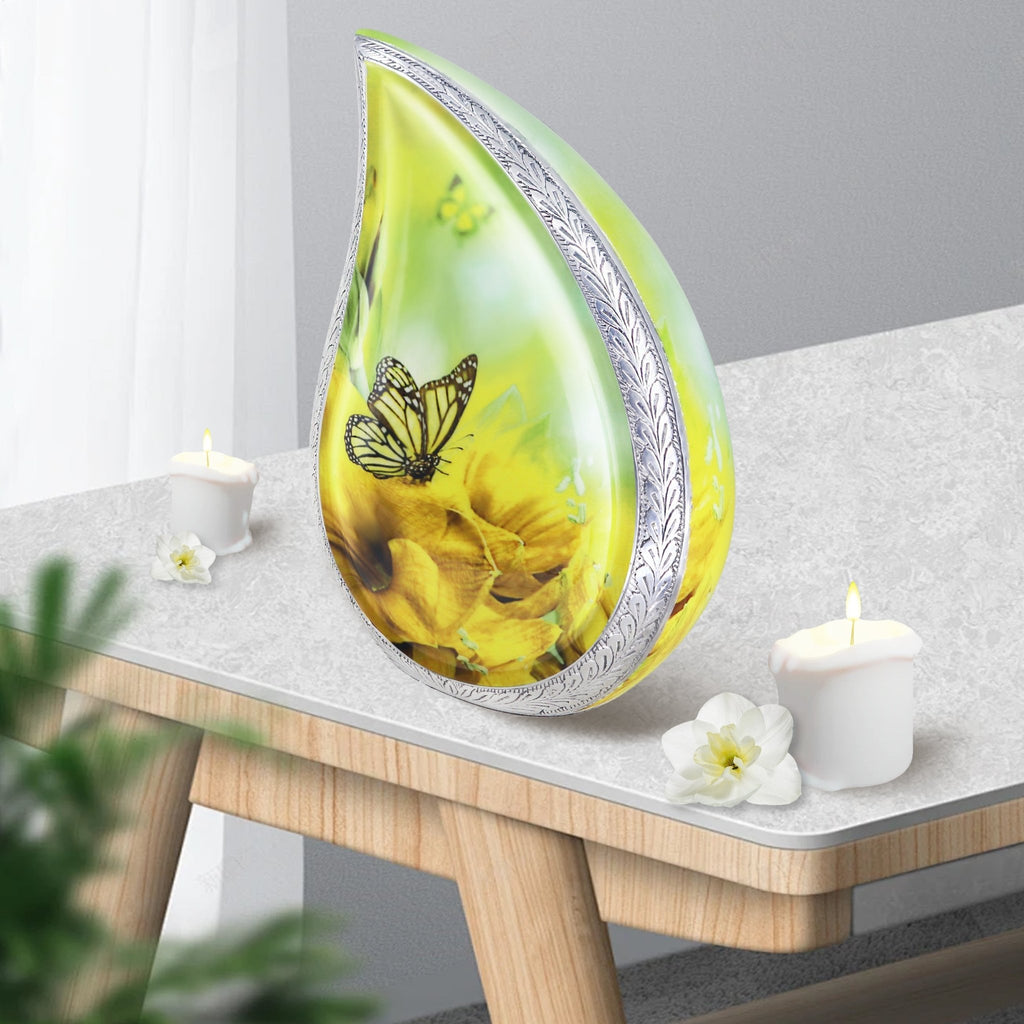 Sunflower butterfly metal burial urns teardrop shaped placed on wooden side table with candles for home mantel decor