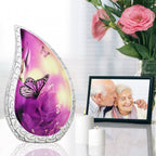 Pink butterfly metal ash urn laid on reflective table beside family photo frame and gentle memorial blossom decor