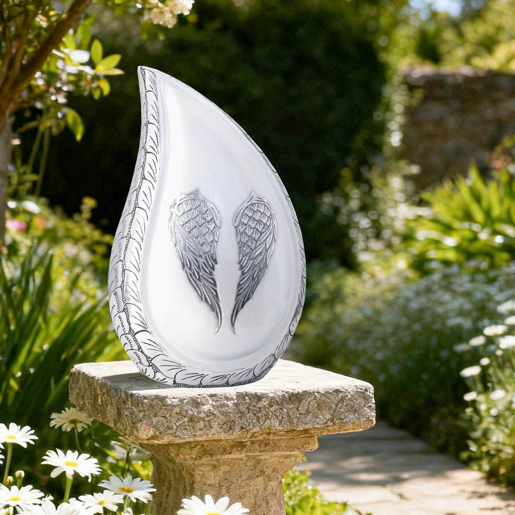 Elegant white angel wing teardrop cremation urns for adults resting on stone garden pillar for cemetery remembrance