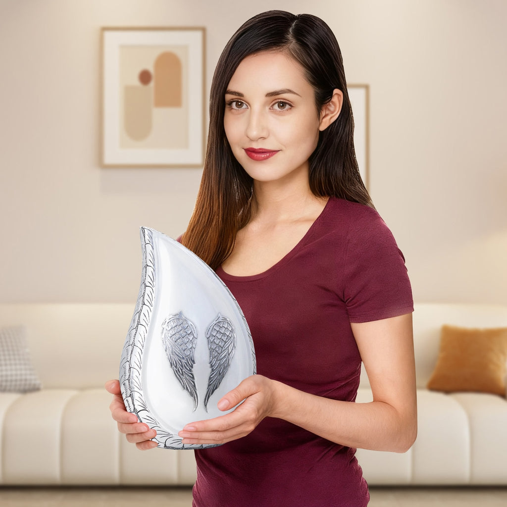 Female holding large white engraved angel wing teardrop urns for ashes aluminum memorial vessel in living room