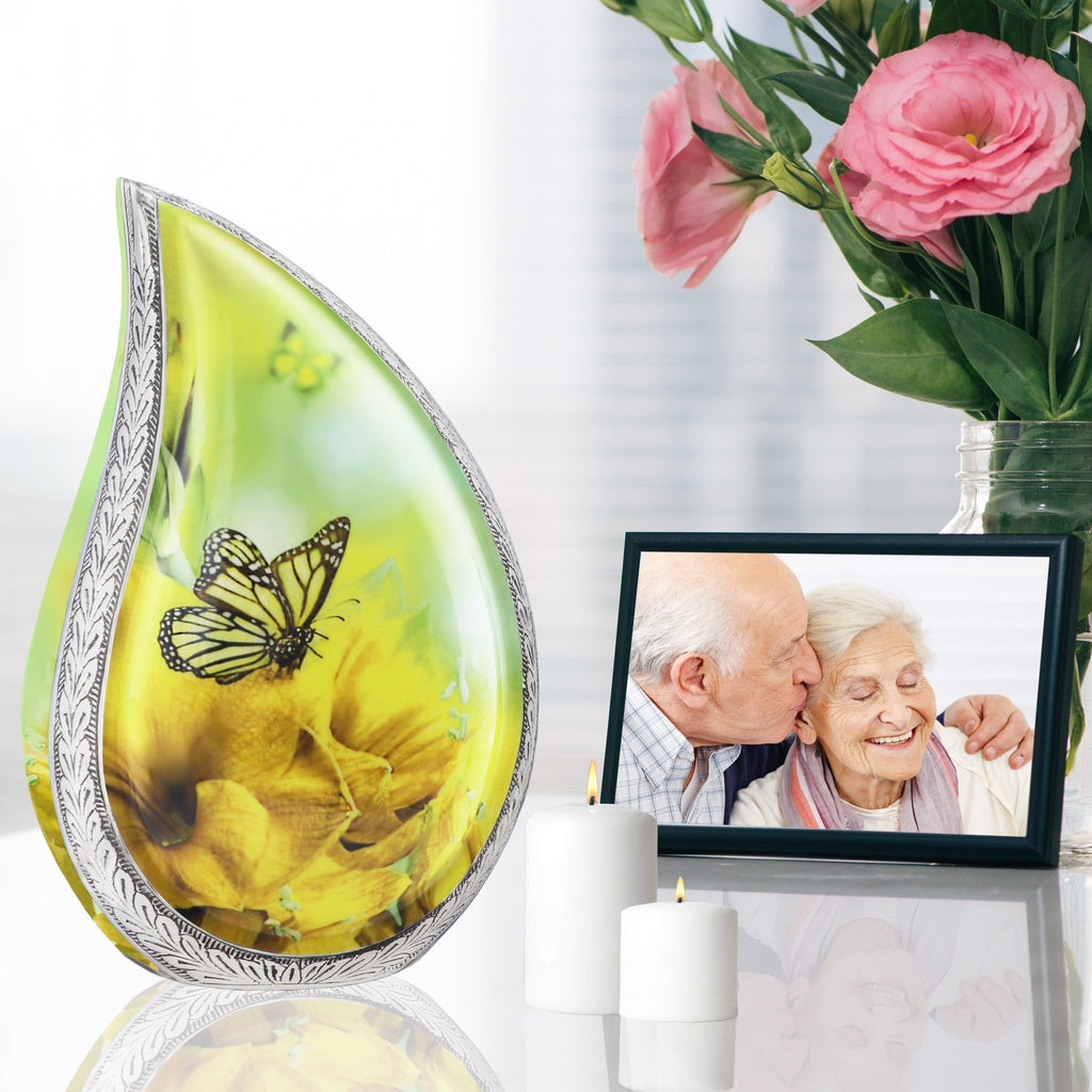 Yellow sunflower butterfly cremation urns for adults set on reflective table with family photo and soft pink blooms
