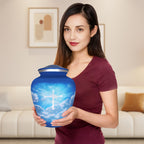 Woman holding a large blue sky cross urn for ashes, showing the full-size adult memorial urn for scale