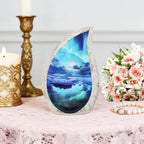 Ocean wave brass teardrop ash urn set on lace tablecloth with gold candlesticks and pink funeral rose bouquet