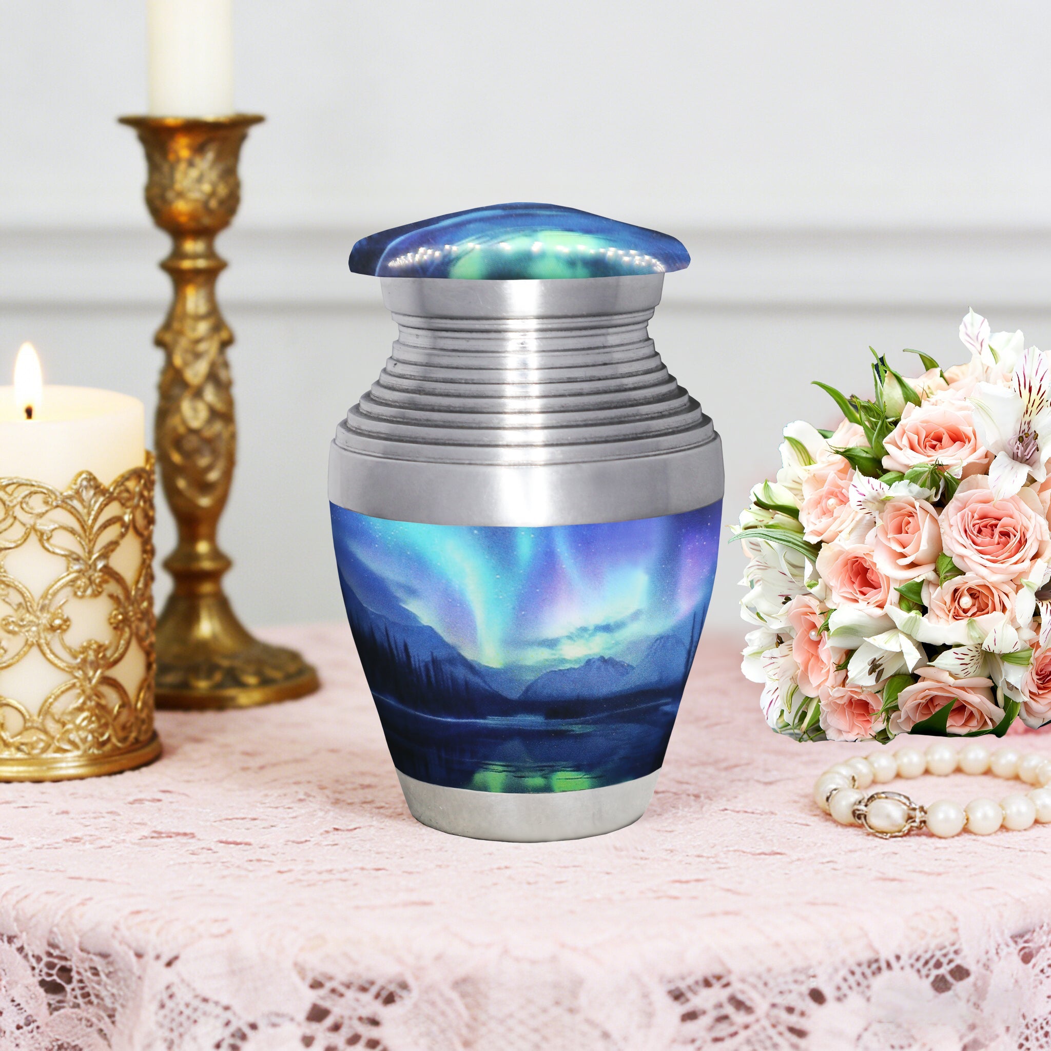 Miniature urn for ashes with Aurora Borealis artwork displayed with memorial flowers and an elegant gold candlestick
