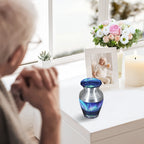 Metal keepsake urn for cremated remains with turquoise Aurora artwork displayed near an elderly woman at home