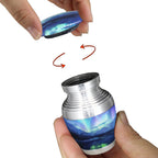 Mini urn for ashes with Northern Lights artwork and secure threaded screw-top lid shown opened by hand