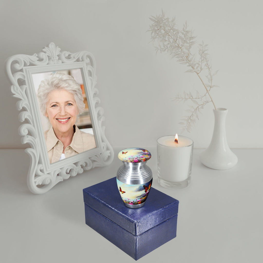 Cremation containers with butterfly sky design, small memorial urn with screw lid, displayed with photo frame and candle