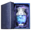 Metal keepsake urn for ashes with blue cosmic galaxy artwork presented in a padded blue memorial gift box