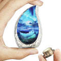 Brass keepsake urn for ashes with turquoise Aurora Borealis artwork held in one hand beside its bottom-threaded lid