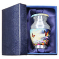 Keepsake urn with colorful butterfly and flower artwork, small memorial vessel presented in a blue satin gift box