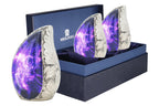 Set of 3 mini urns for ashes with purple cosmic galaxy artwork arranged in a blue presentation box