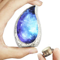 Brass keepsake urn for ashes with black and blue cosmic galaxy artwork held in one hand beside its bottom-threaded lid