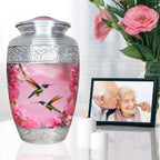 Pink hummingbird funeral urn displayed beside flowers and a framed memorial photo for peaceful remembrance