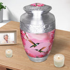 Floral hummingbird cremation urn displayed with candles and a family photo for an elegant home memorial