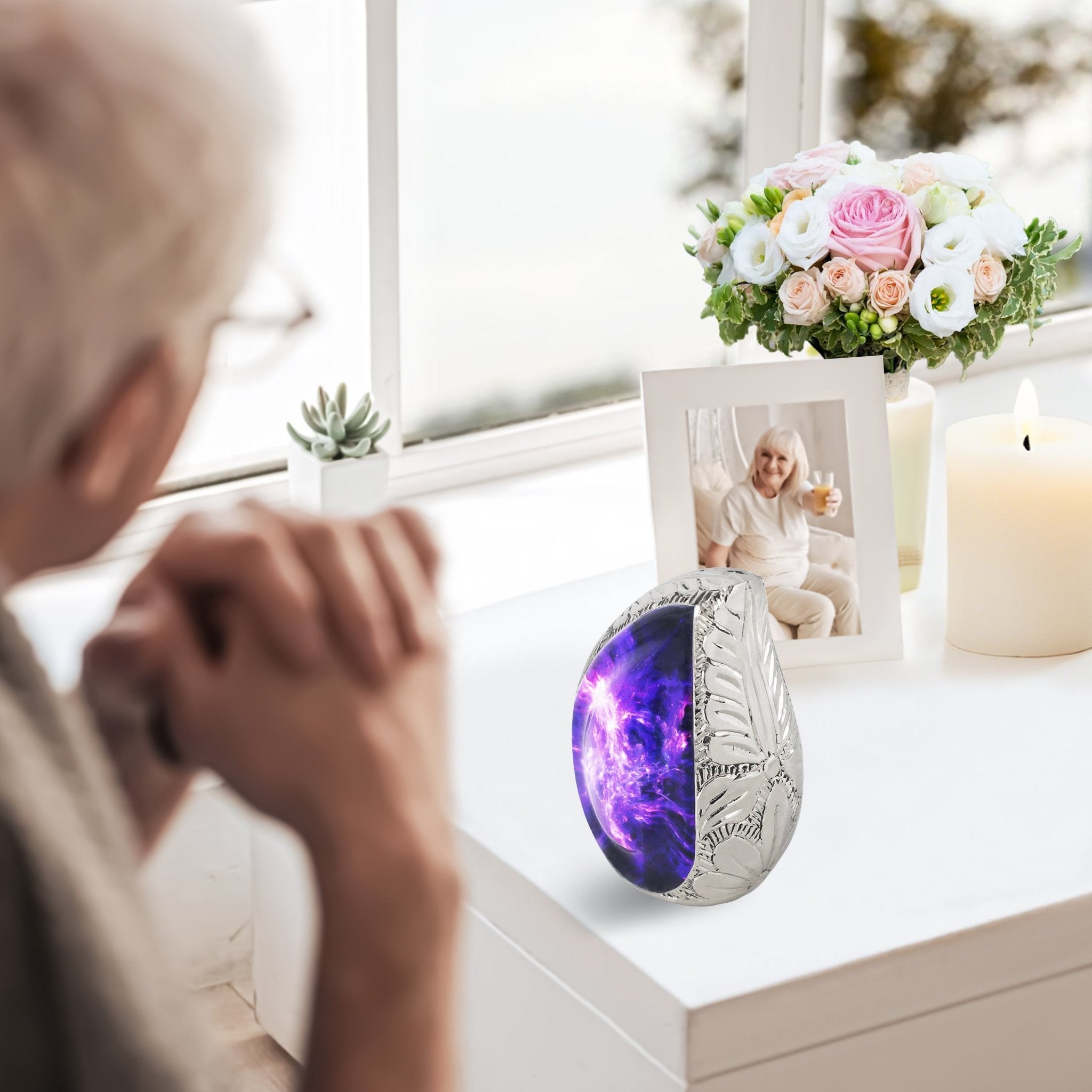 Small keepsake urn with purple galaxy artwork displayed near an elderly woman in a peaceful home memorial