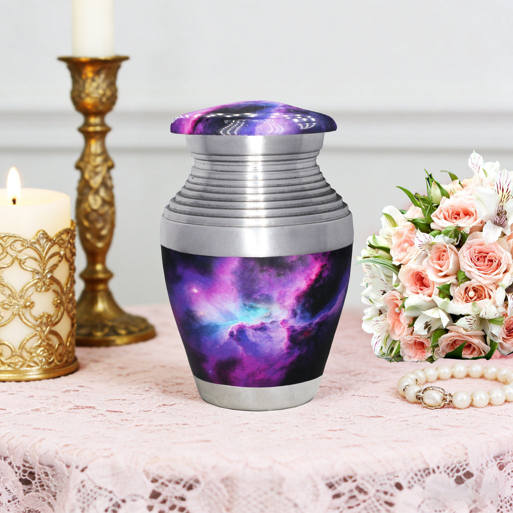 Tiny urn for ashes with purple cosmic galaxy print displayed with flowers and an elegant gold candlestick