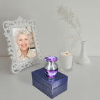 Keepsake urns for ashes with cosmic galaxy artwork displayed on a blue presentation box beside a memorial portrait