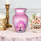 Small urns for ashes featuring a pink Tree of Life, displayed with candles and flowers for dad's remembrance