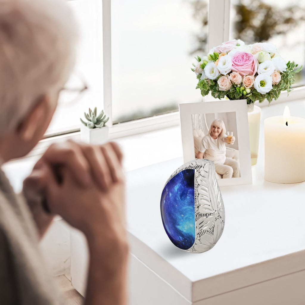 Lifestyle mantel view, blue galaxy brass tiny funeral urn displayed beside family photo for loved one remembrance