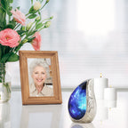 Glossy vanity table holding blue starry brass miniature ash urn beside pink blossoms for quiet home memorial display