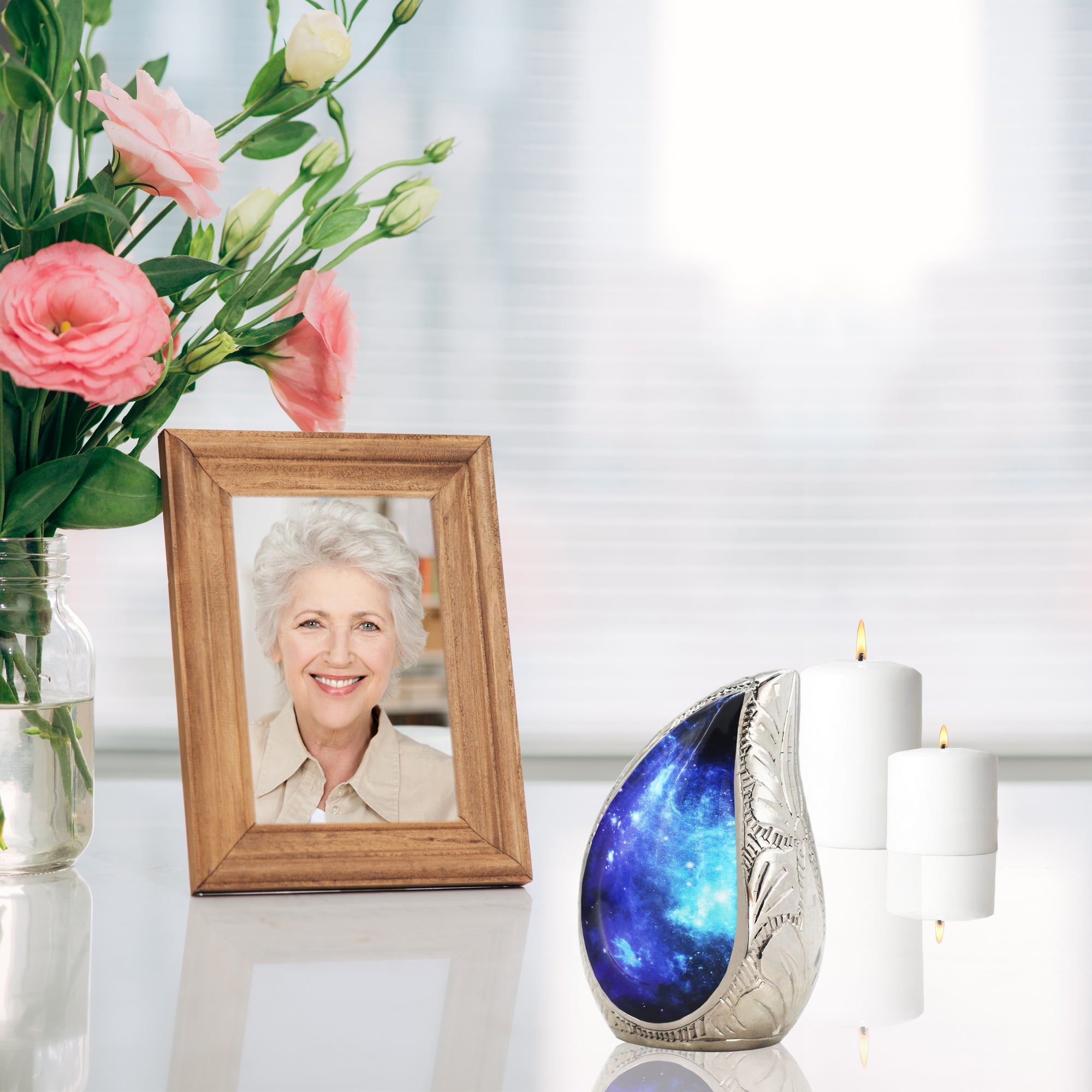 Glossy vanity table holding blue starry brass miniature ash urn beside pink blossoms for quiet home memorial display