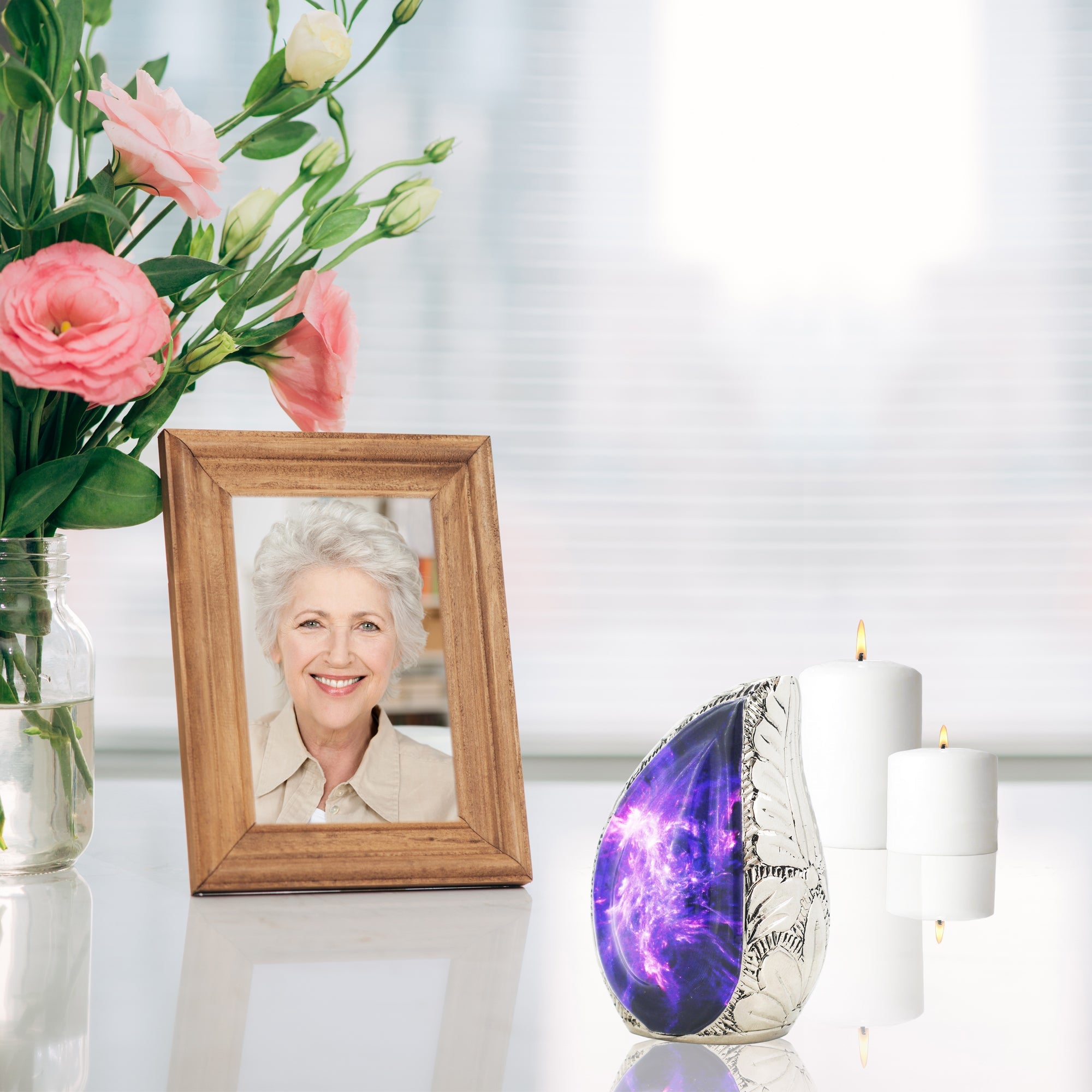 Vintage styled purple nebula brass micro cremation urn displayed on reflective table with pink blooms and memorial portrait