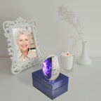 Purple starry brass tiny ash keepsake urn resting on navy gift box next to framed photo and memorial candle