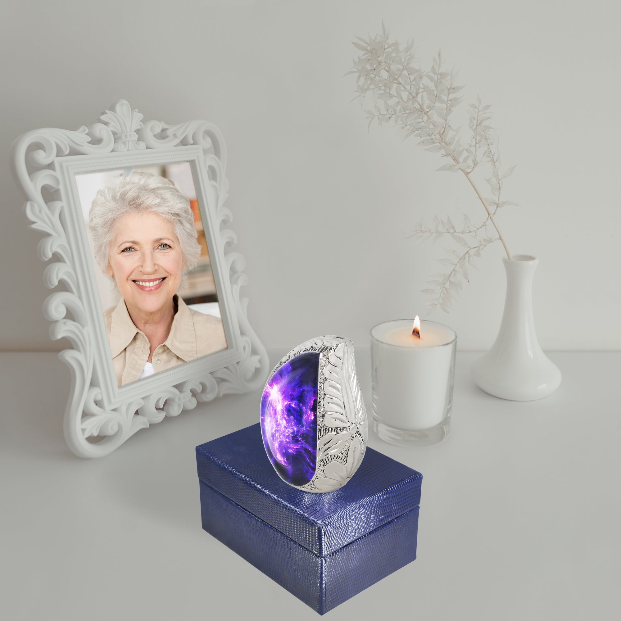 Purple starry brass tiny ash keepsake urn resting on navy gift box next to framed photo and memorial candle