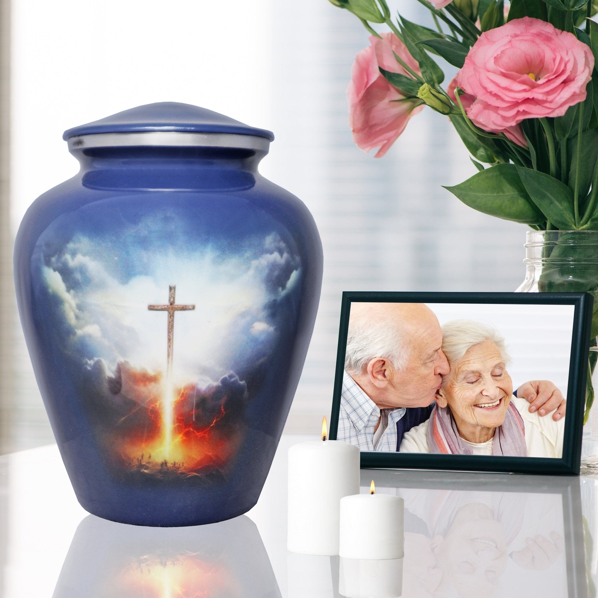 Funeral urn with glowing Cross of Life design displayed beside pink flowers and a framed family memorial photo